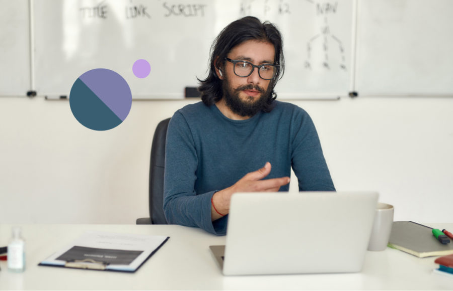 A tan man with should-length black hair and beard sitting at a desk in a data science bootcamp
